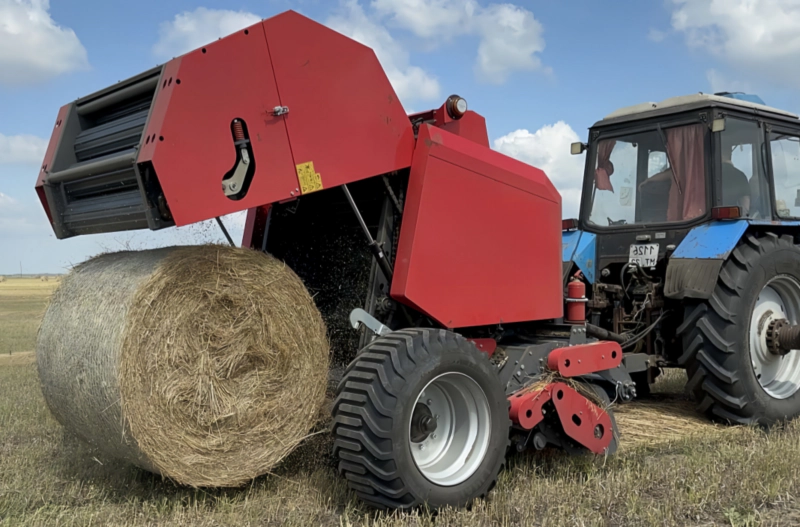 A round baler is baling crops in the field.